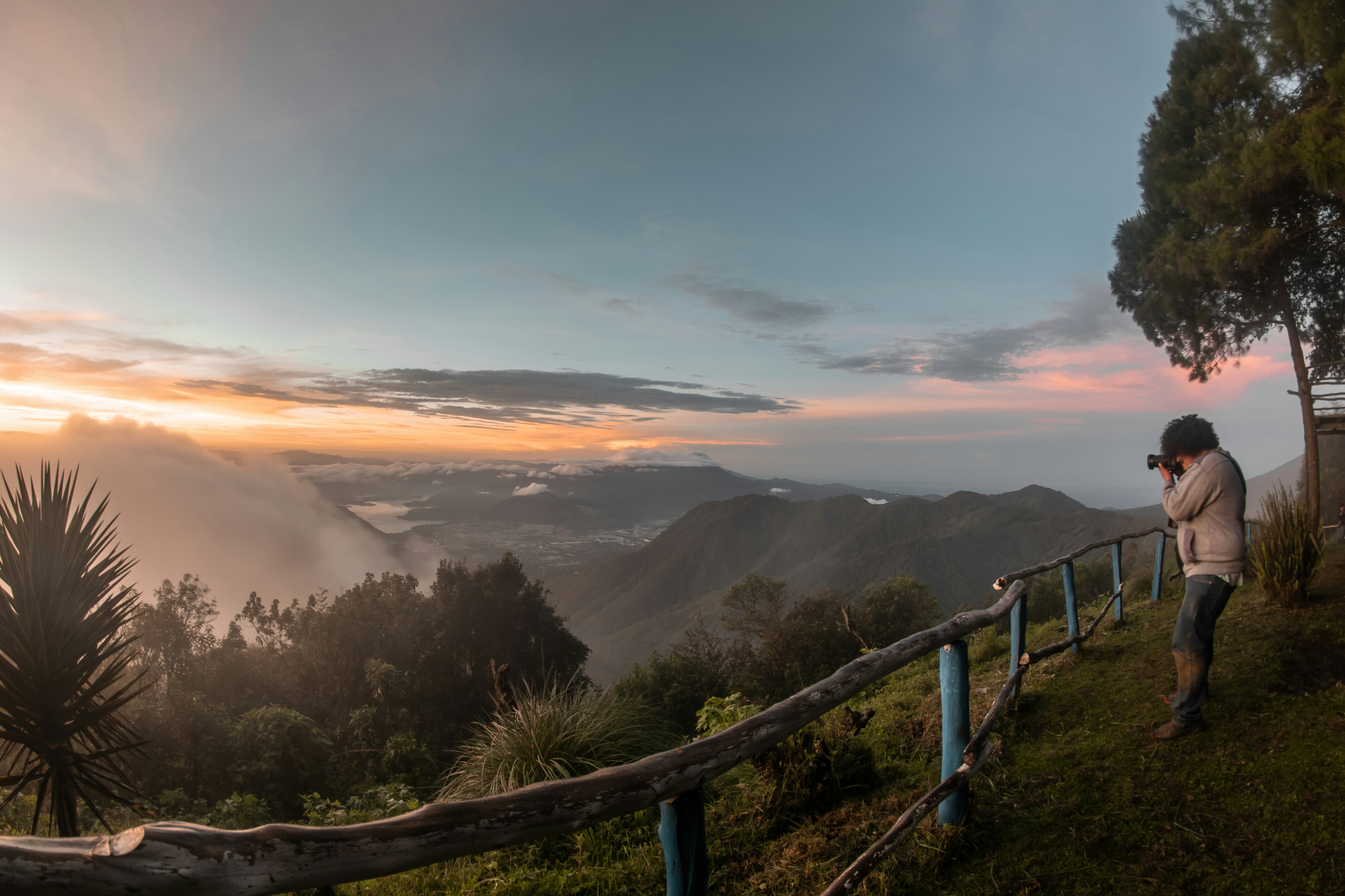 man taking photo of orange sunset scene over hills