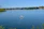 Person kayaking on a calm lake surrounded by lush greenery under a clear sky.