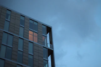 A sleek, modern office building facade at dusk with warm interior lights glowing.