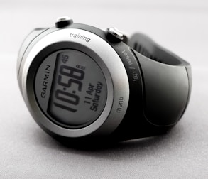A sleek and modern digital wristwatch displaying the time 10:58. The watch has a round face with a metallic silver and black casing. Various buttons are visible on the sides, labeled 'training', 'lap/reset', and 'menu'. The watch is on a light gray, textured background.