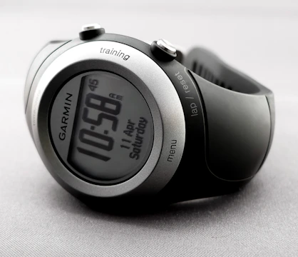 A sleek and modern digital wristwatch displaying the time 10:58. The watch has a round face with a metallic silver and black casing. Various buttons are visible on the sides, labeled 'training', 'lap/reset', and 'menu'. The watch is on a light gray, textured background.