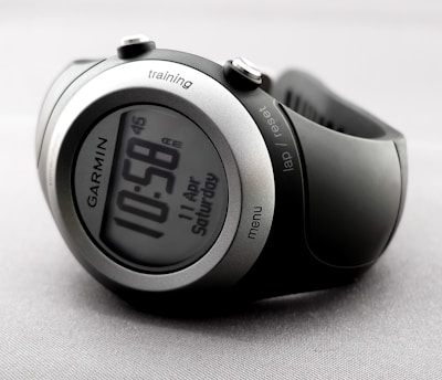 A sleek and modern digital wristwatch displaying the time 10:58. The watch has a round face with a metallic silver and black casing. Various buttons are visible on the sides, labeled 'training', 'lap/reset', and 'menu'. The watch is on a light gray, textured background.