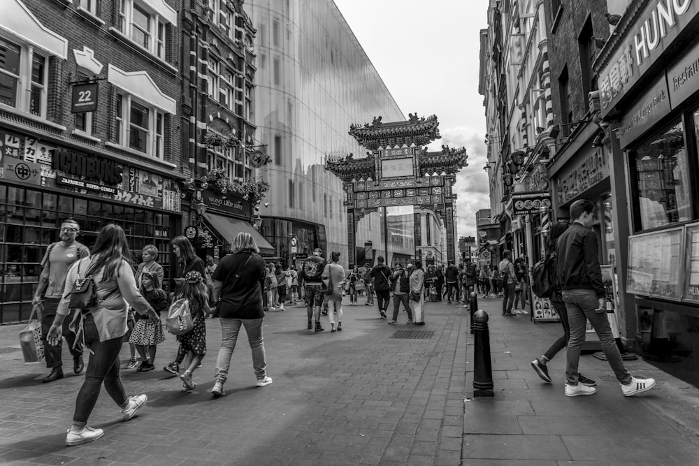 greyscale photography of people walking on street between buildings