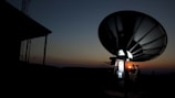Technicians installing satellite dishes on a rooftop at sunset.