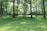 A lush, green park with tall trees casting dappled shadows on the grass. A person is practicing yoga or stretching in the open space surrounded by the serenity of nature.