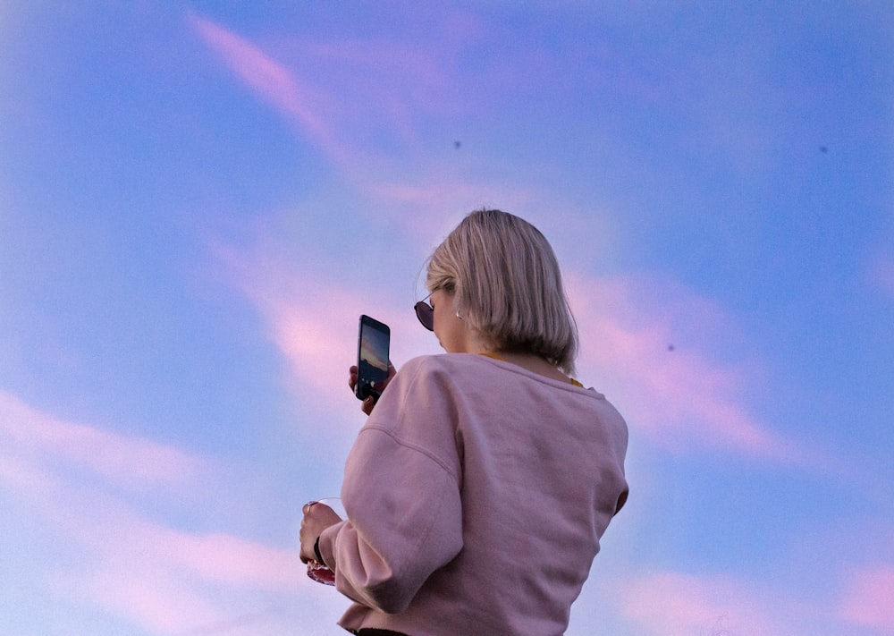 Frau mit Sonnenbrille und rosa Oberteil hält Telefon in der Hand