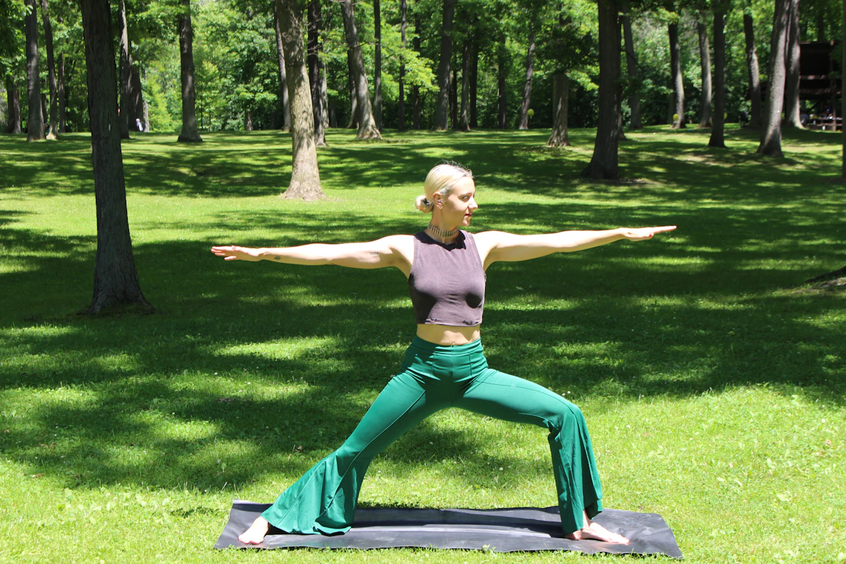 Woman practicing a Virabhadrasana Warrior Pose variation outdoors in a forest, lunging with arms extended