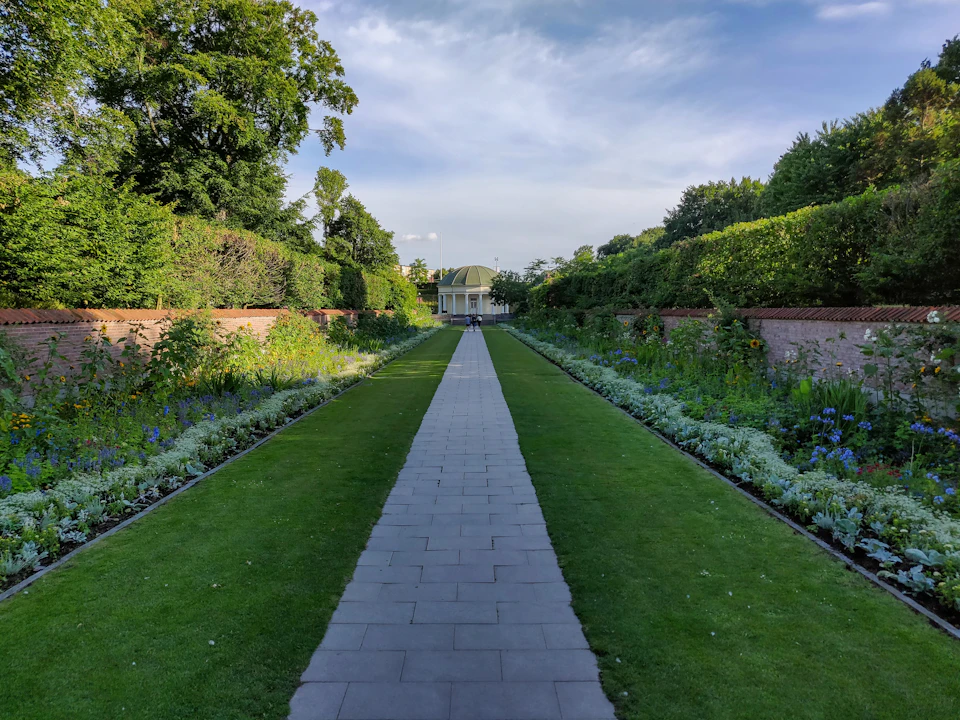 Serene garden path winds through lush greenery and vibrant flowers under a clear blue sky