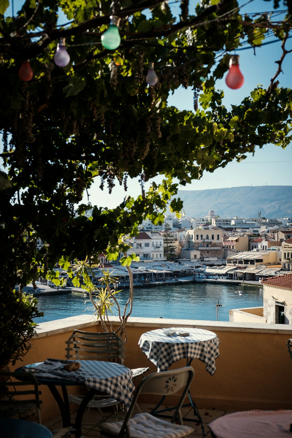 tafeltjes op een balkon met een boom, met uitzicht over de zee en de stad