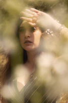Soft-focus image of a woman wearing a delicate necklace, smiling gently in natural sunlight.