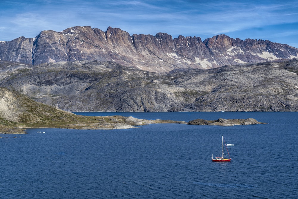 青と白の空の下で灰色の山を眺める青い海に浮かぶ赤いボート