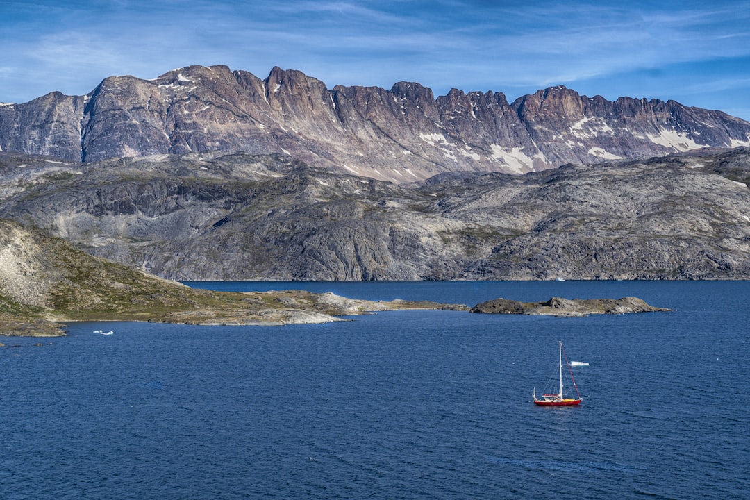 red boat on blue sea viewing gray mountain under blue and white skies,