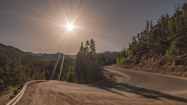 A serene mountain road winding through lush green forests under a clear blue sky.