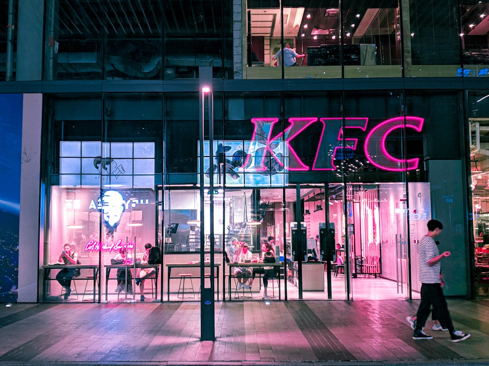 duas pessoas caminhando perto do prédio do KFC durante a noite