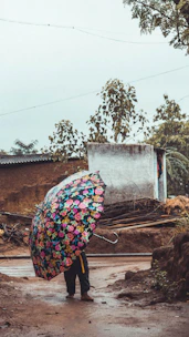 A wide, sturdy umbrella open under a summer drizzle with bright floral patterns.