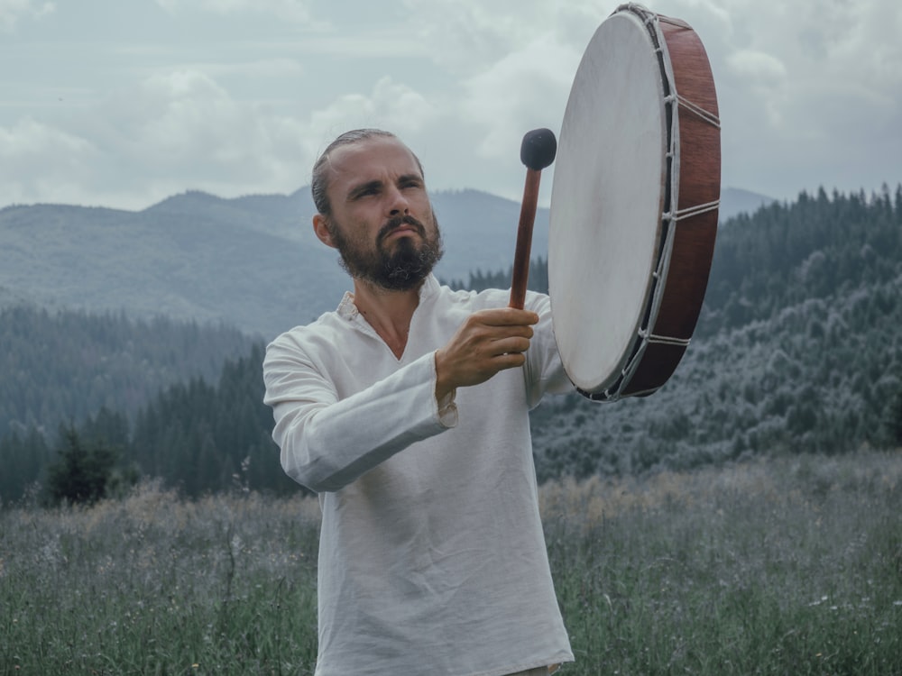 Hombre tocando instrumento de percusión en el campo de hierba cerca del bosque