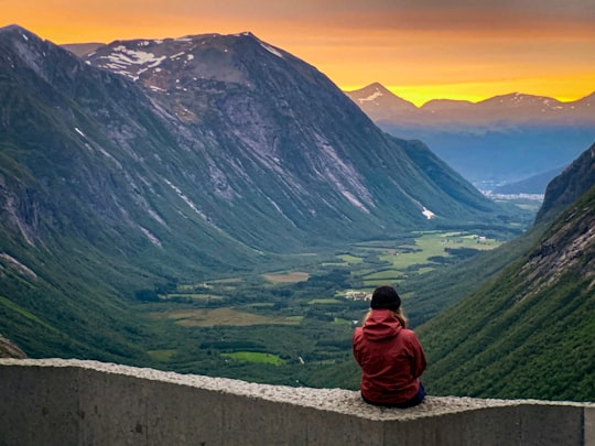 woman wearing red hoodie sitting on concrete with view of valley in Trollstigen Norway