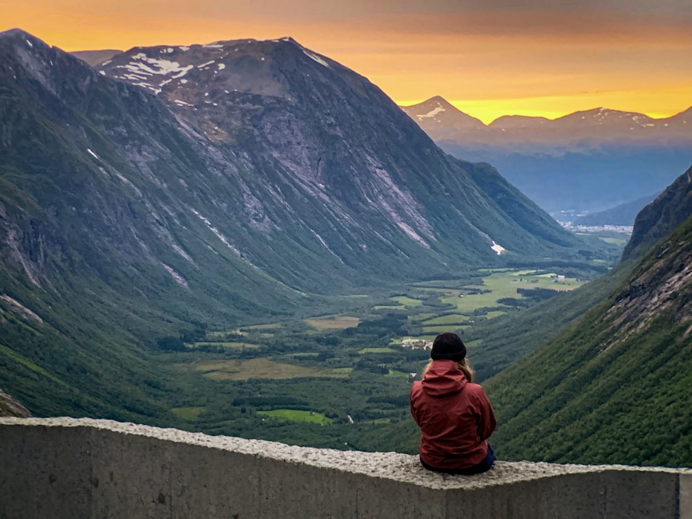 woman wearing red hoodie sitting on concrete with view of valley