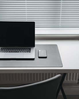 A minimalist workspace with a laptop and pastel-colored phone cases on a wooden desk.