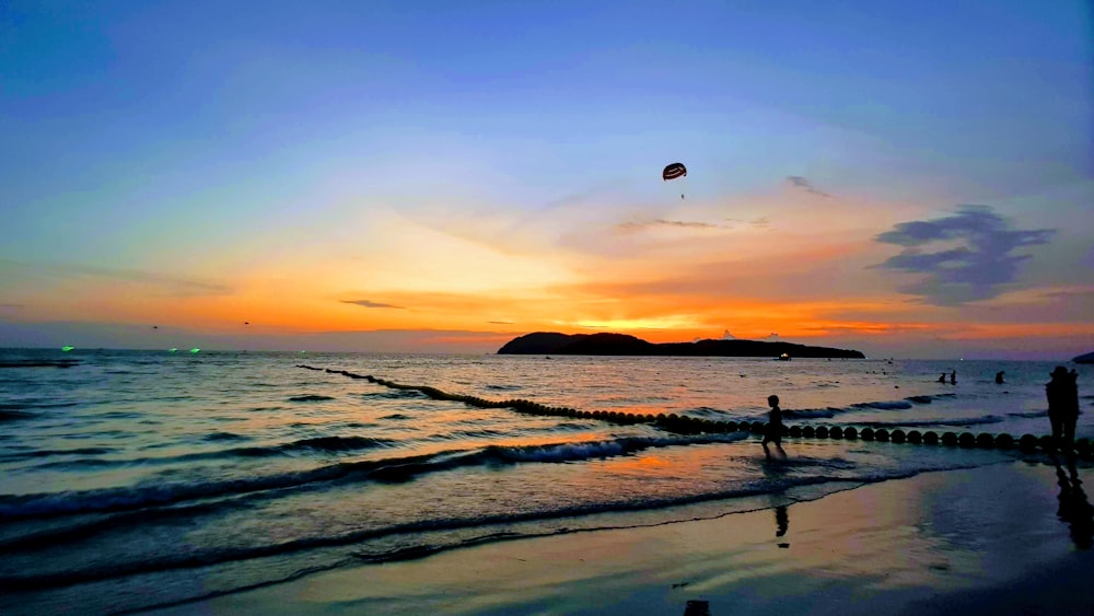 Pessoas na praia sob o céu laranja ao pôr do sol