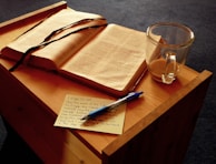 An open book with handwritten notes and a cup of tea on a rustic wooden desk.