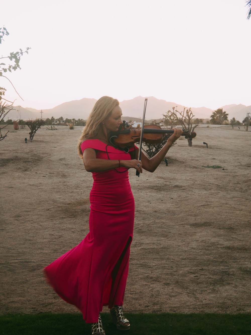 Mujer de pie y tocando el violín en el campo marrón