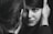 A close-up black and white photograph capturing a woman gazing intently at the camera, framed by a man's hand gently holding her face. The focus is on her expressive eyes and subtle smile, creating an intimate and personal atmosphere.