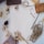 A collection of craft materials including twine, a paintbrush, wooden clothespins, fabric swatches, a pinecone, red beads, and a roll of tape are arranged on a white surface.
