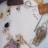 A collection of craft materials including twine, a paintbrush, wooden clothespins, fabric swatches, a pinecone, red beads, and a roll of tape are arranged on a white surface.