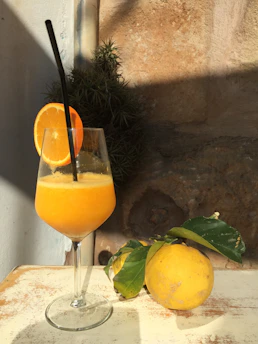 Bright orange juice with slices of citrus fruits and a straw on a wooden table
