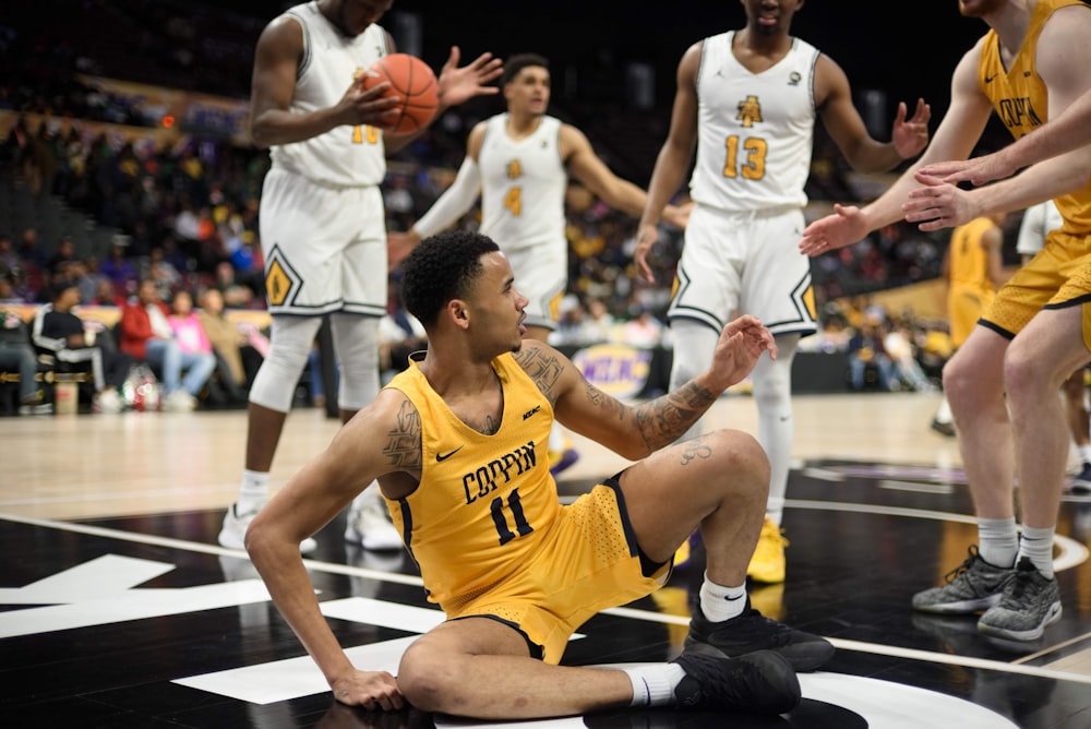 man in yellow 11 basketball uniform sitting on middle of court surrounded by other players