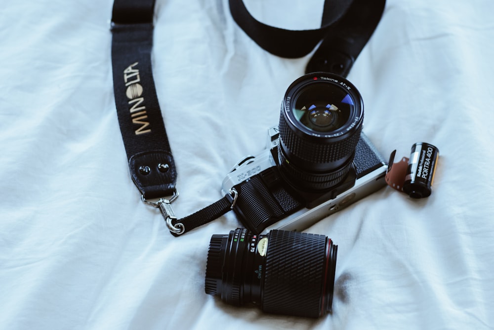 black and gray SLR camera beside lens on white textile