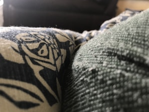 A close-up view of a textured fabric with a printed design in contrasting colors. The texture is detailed, showing fibers and small particles on the surface.