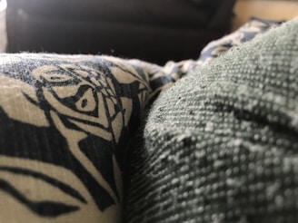 A close-up view of a textured fabric with a printed design in contrasting colors. The texture is detailed, showing fibers and small particles on the surface.