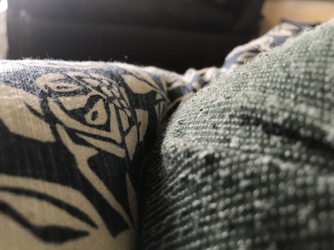 A close-up view of a textured fabric with a printed design in contrasting colors. The texture is detailed, showing fibers and small particles on the surface.