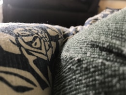 A close-up view of a textured fabric with a printed design in contrasting colors. The texture is detailed, showing fibers and small particles on the surface.