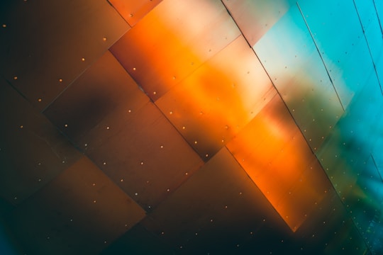 A series of metallic panels with a gradient of orange and teal colors, each panel is riveted and slightly reflective.