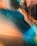 A close-up view of a metallic surface with a smooth, curving design. The material reflects light in a gradient of colors including copper, blue, and teal, creating an abstract, artistic appearance. There are visible rivets evenly spaced across the panels, adding texture to the surface.