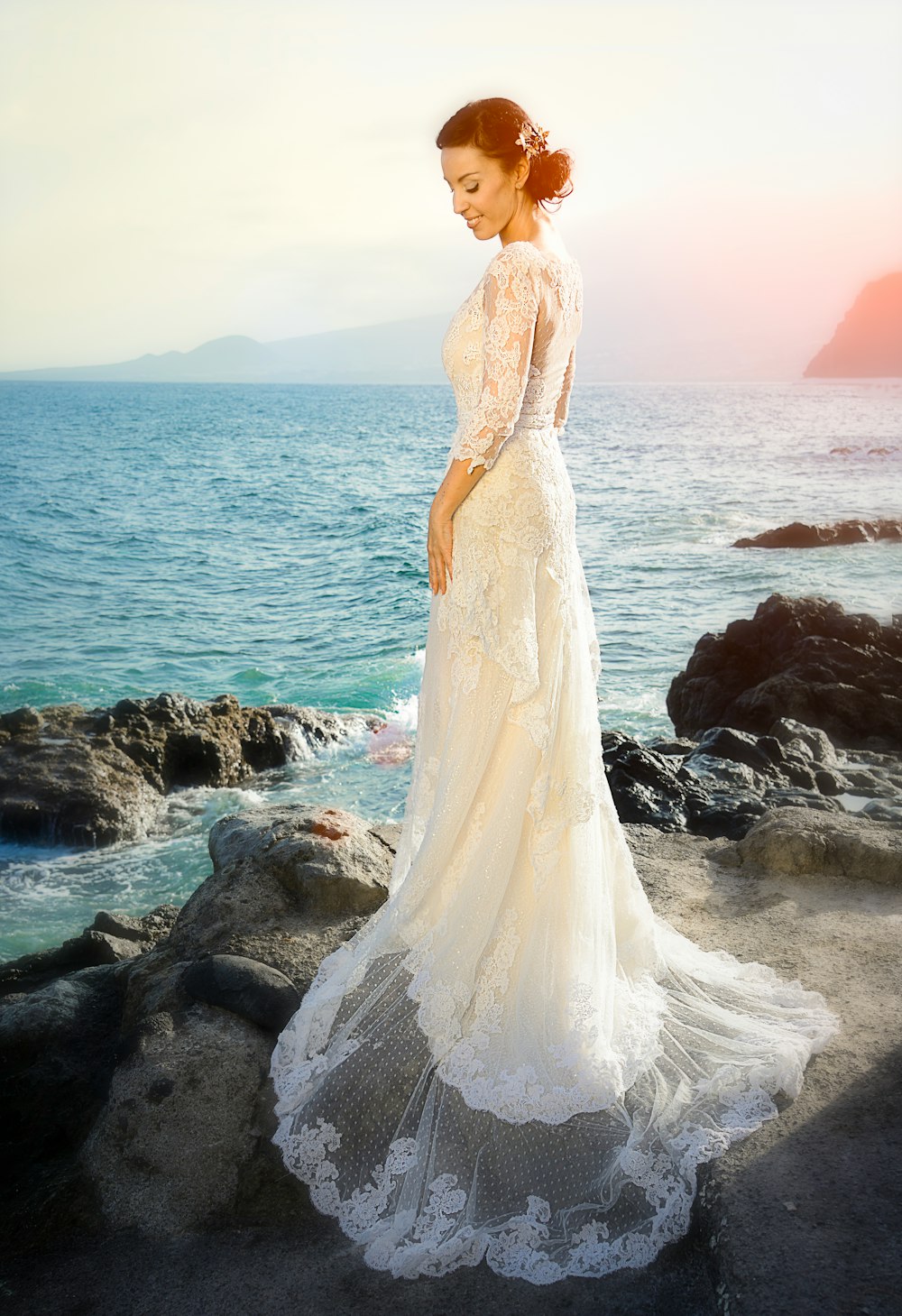 woman wearing white gown standing on rocks across body of water