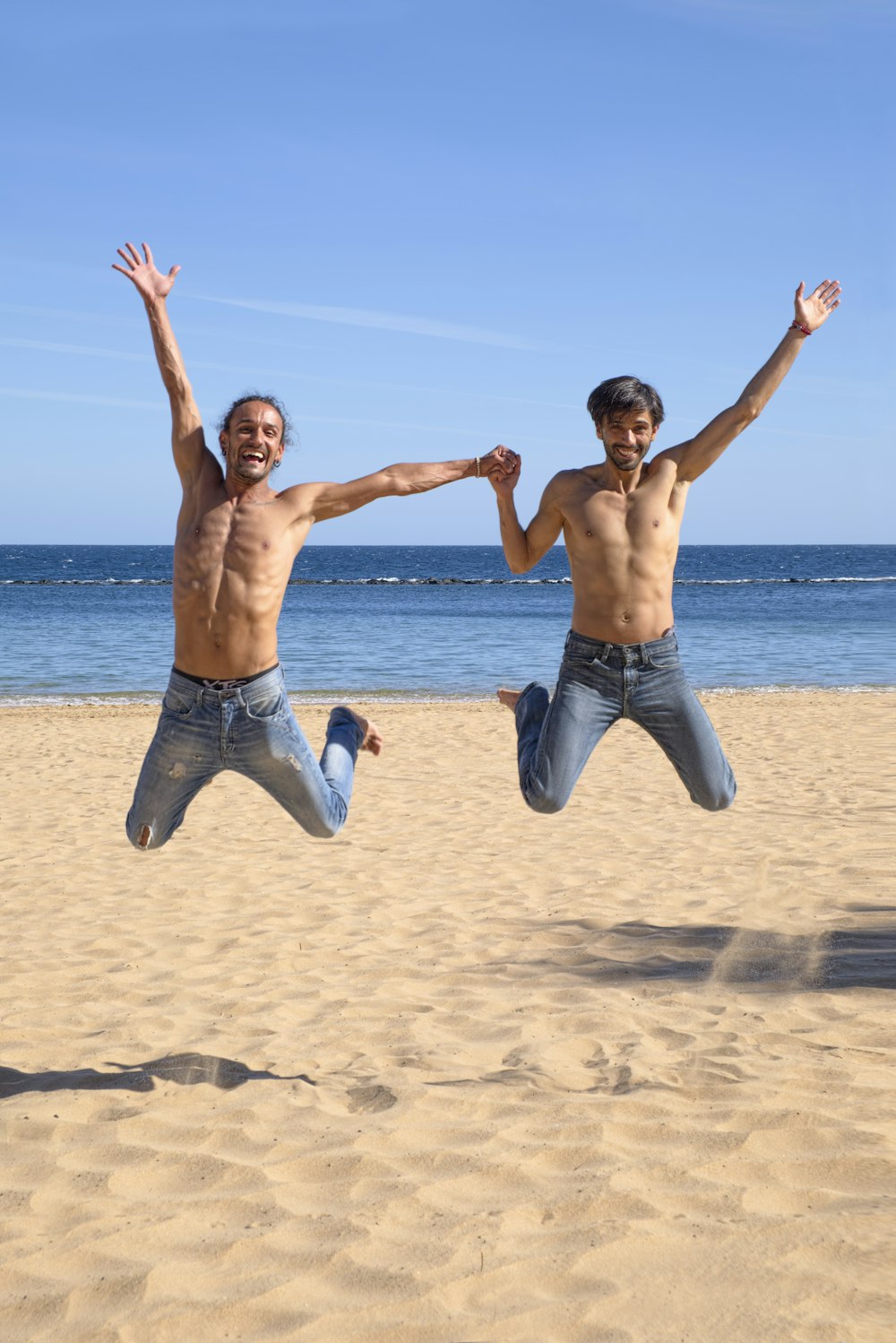 Zwei Männer springen über braunen Strandsand