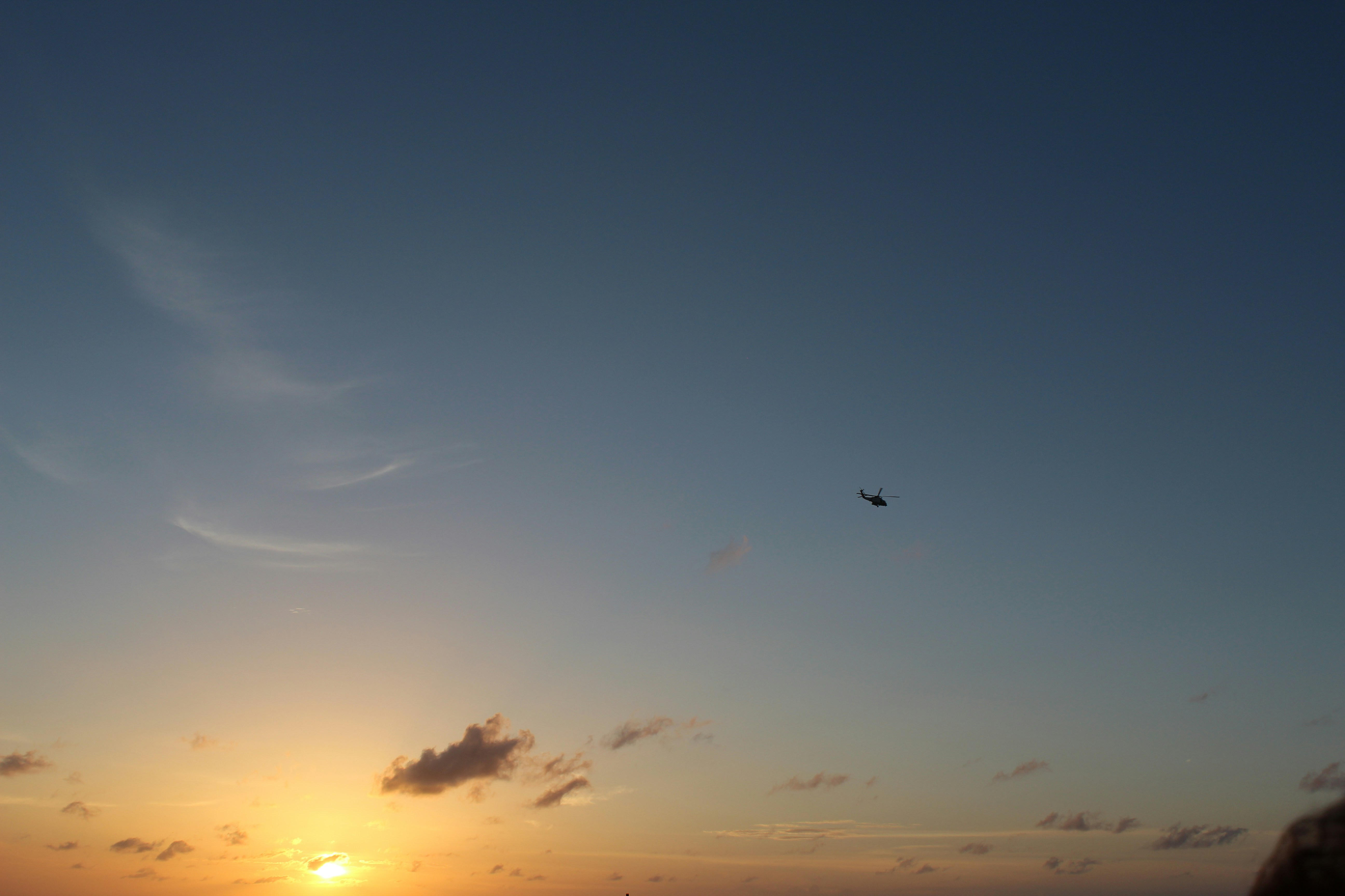Helicopter silhouette against twilight sky, mountain peaks in background, dark atmospheric mood, purple-blue tones