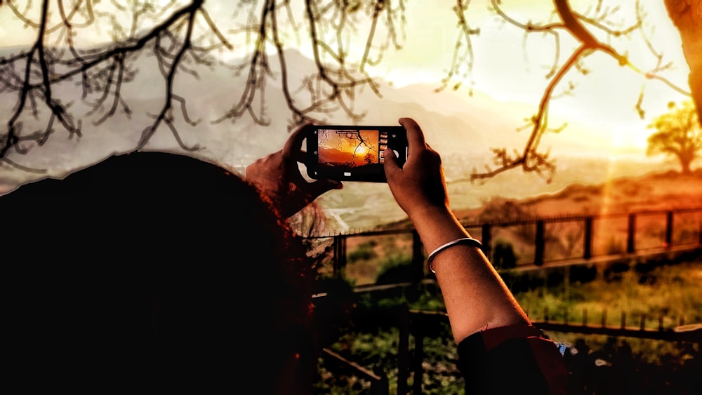 person taking a picture of the sun using smartphone during golden hour