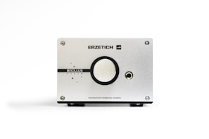 A sleek, minimalist headphone amplifier with a silver metallic finish. It features the brand name 'Erzetich' at the top and 'Bacillus Tilia' below a central large knob. A headphone jack is visible on the right side. The device is sturdy, with screws at each corner and a clean, industrial design aesthetic.