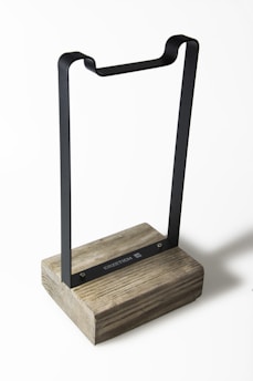 A metal stand with a wooden base featuring clean lines and a minimalist design. The metal frame is black and rectangular, while the wooden base has a natural, rustic texture.