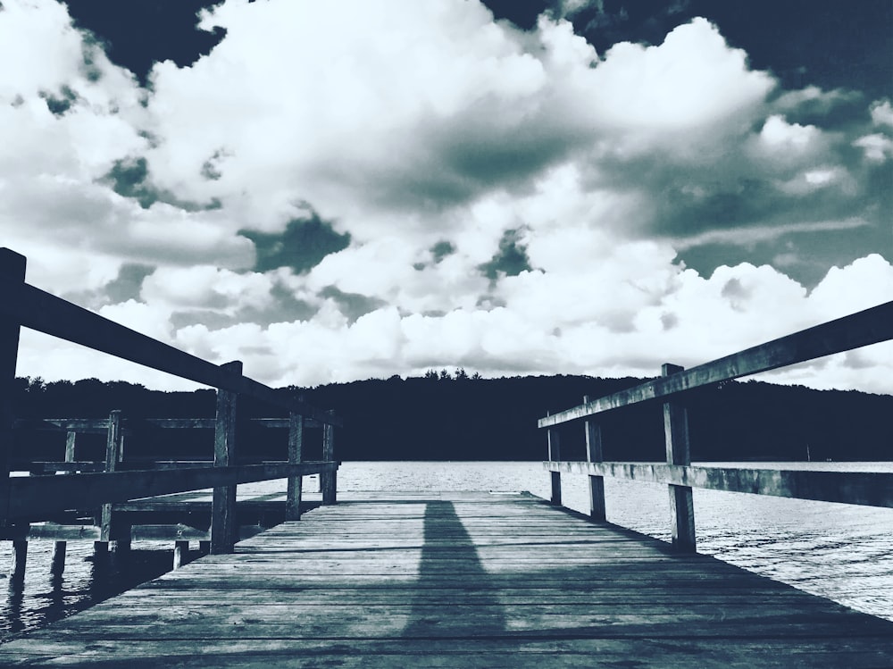 grayscale photography of boardwalk under cloudy sky