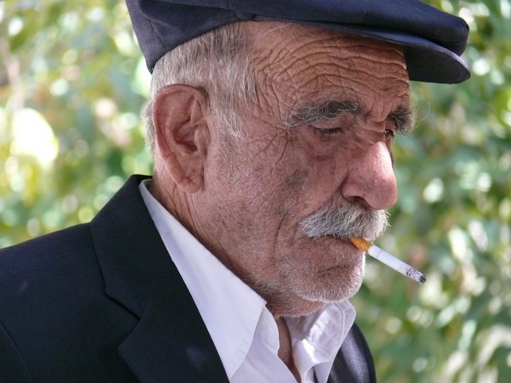 man in black suit jacket and cap smoking cigarette