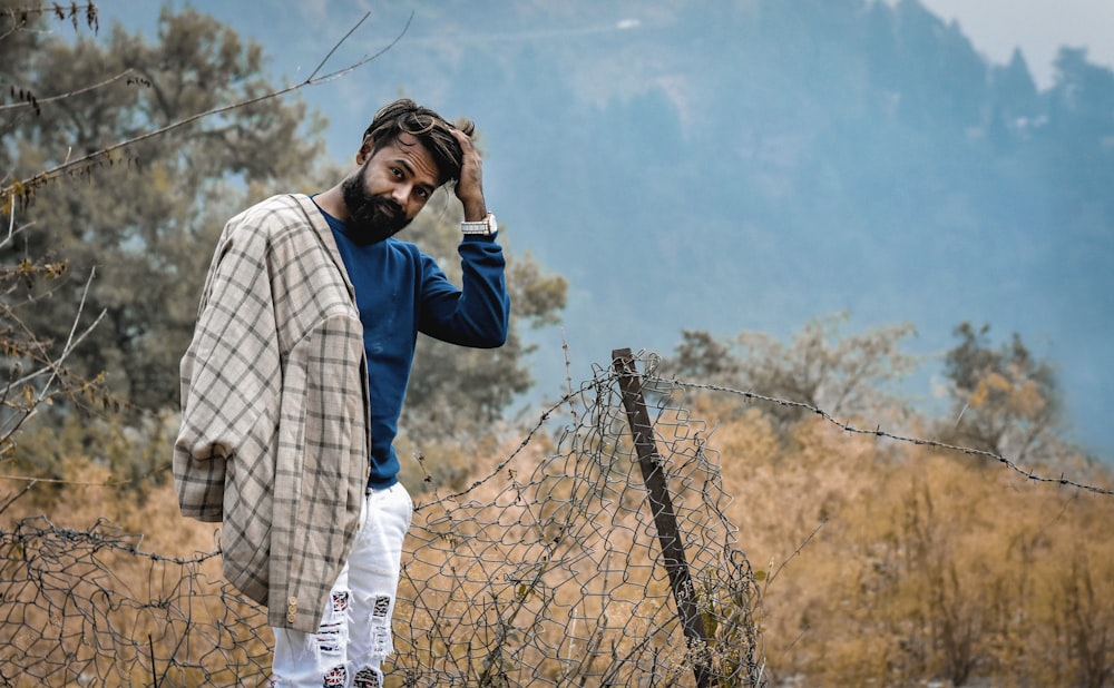 man in blue sweater and white distressed denim jeans with brown plaid shirt draped over shoulder