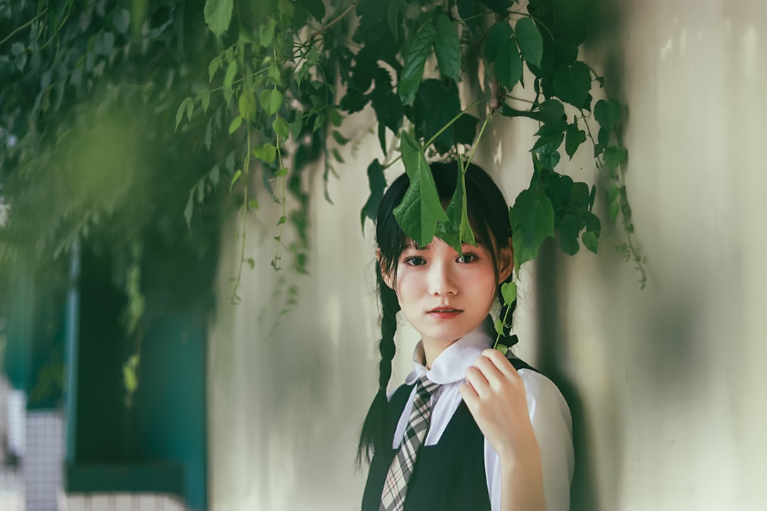 woman in black and white school uniform standing under green leafy vine beside wall