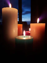 Candles of various sizes and colors lit softly on a windowsill during an evening event.