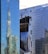 A modern urban landscape featuring high-rise buildings with glass facades. The reflections of the surrounding architecture are visible on the windows, creating a distorted and dynamic visual effect. A construction crane can be seen in the background, suggesting ongoing development in the area.